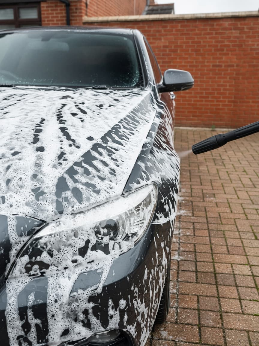 Snow foam being rinsed from a dark car